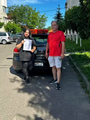 Cursant admis la examenul auto, cu foaia în mână, lângă mașina școlii