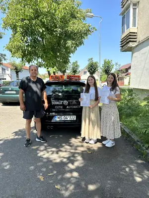 Cursant admis la examenul auto, cu foaia în mână, lângă mașina școlii