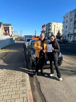 Cursant admis la examenul auto, cu foaia în mână, lângă mașina școlii