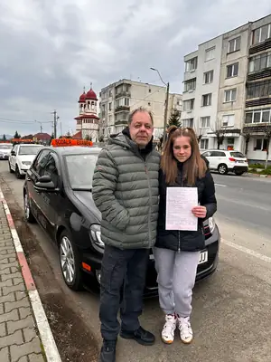 Cursant admis la examenul auto, cu foaia în mână, lângă mașina școlii