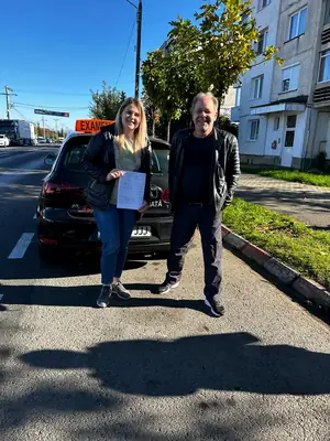 Cursant admis la examenul auto, cu foaia în mână, lângă mașina școlii