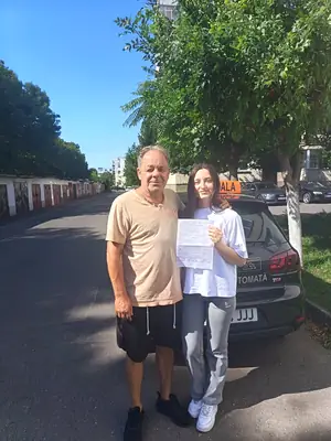 Cursant admis la examenul auto, cu foaia în mână, lângă mașina școlii