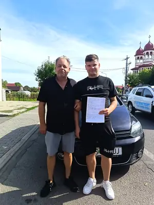 Cursant admis la examenul auto, cu foaia în mână, lângă mașina școlii