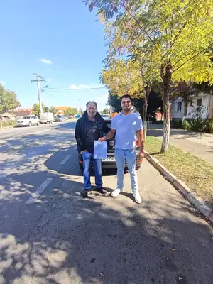 Cursant admis la examenul auto, cu foaia în mână, lângă mașina școlii