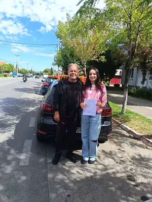 Cursant admis la examenul auto, cu foaia în mână, lângă mașina școlii