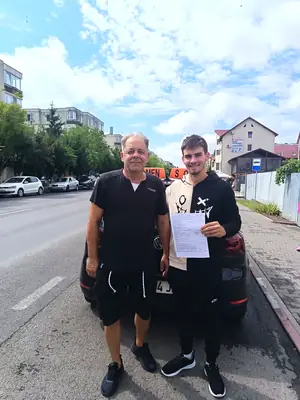 Cursant admis la examenul auto, cu foaia în mână, lângă mașina școlii