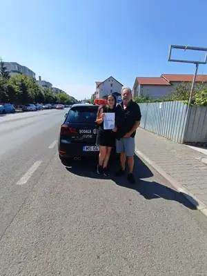 Cursant admis la examenul auto, cu foaia în mână, lângă mașina școlii