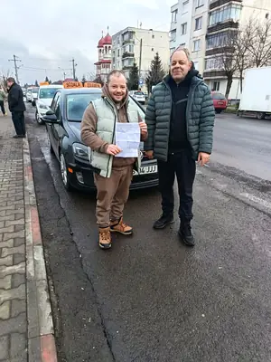 Cursant admis la examenul auto, cu foaia în mână, lângă mașina școlii