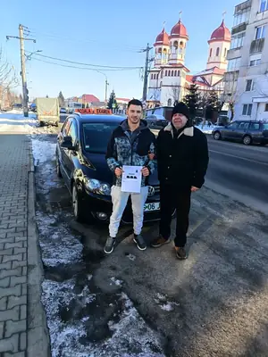 Cursant admis la examenul auto, cu foaia în mână, lângă mașina școlii