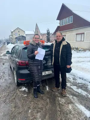 Cursant admis la examenul auto, cu foaia în mână, lângă mașina școlii
