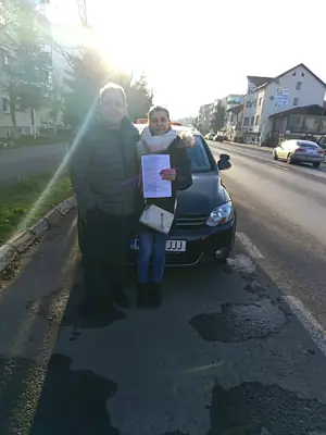 Cursant admis la examenul auto, cu foaia în mână, lângă mașina școlii