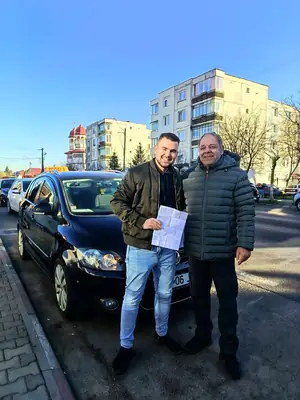 Cursant admis la examenul auto, cu foaia în mână, lângă mașina școlii