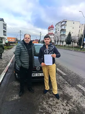 Cursant admis la examenul auto, cu foaia în mână, lângă mașina școlii