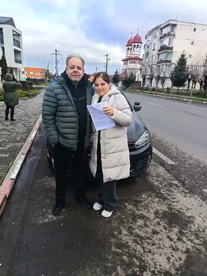 Cursant admis la examenul auto, cu foaia în mână, lângă mașina școlii