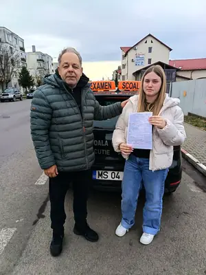 Cursant admis la examenul auto, cu foaia în mână, lângă mașina școlii