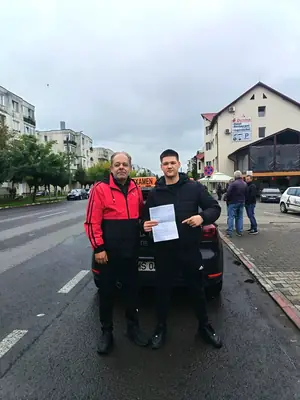 Cursant admis la examenul auto, cu foaia în mână, lângă mașina școlii