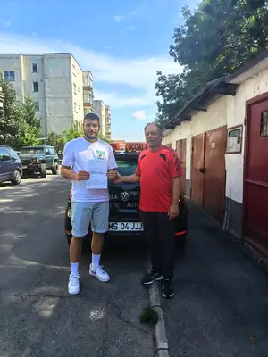 Cursant admis la examenul auto, cu foaia în mână, lângă mașina școlii