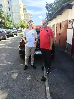 Cursant admis la examenul auto, cu foaia în mână, lângă mașina școlii