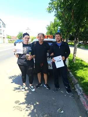 Cursant admis la examenul auto, cu foaia în mână, lângă mașina școlii