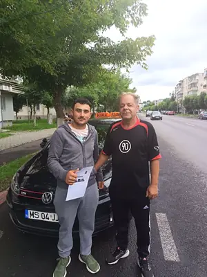 Cursant admis la examenul auto, cu foaia în mână, lângă mașina școlii