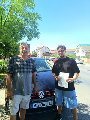 Cursant admis la examenul auto, cu foaia în mână, lângă mașina școlii