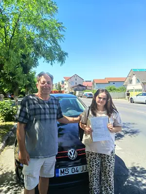 Cursant admis la examenul auto, cu foaia în mână, lângă mașina școlii