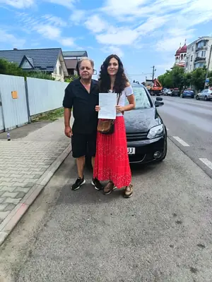 Cursant admis la examenul auto, cu foaia în mână, lângă mașina școlii