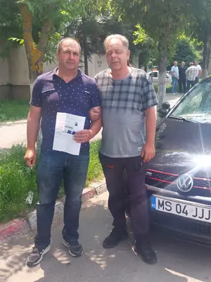 Cursant admis la examenul auto, cu foaia în mână, lângă mașina școlii