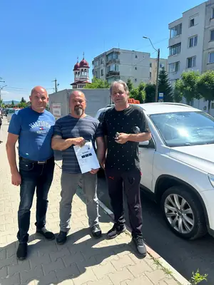 Cursant admis la examenul auto, cu foaia în mână, lângă mașina școlii