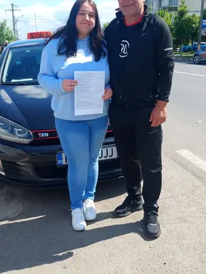 Cursant admis la examenul auto, cu foaia în mână, lângă mașina școlii