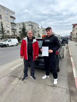 Cursant admis la examenul auto, cu foaia în mână, lângă mașina școlii
