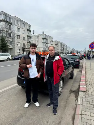 Cursant admis la examenul auto, cu foaia în mână, lângă mașina școlii
