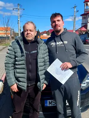 Cursant admis la examenul auto, cu foaia în mână, lângă mașina școlii