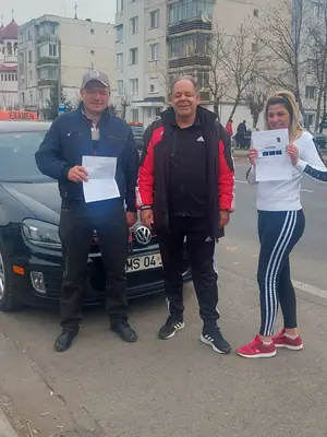 Cursant admis la examenul auto, cu foaia în mână, lângă mașina școlii