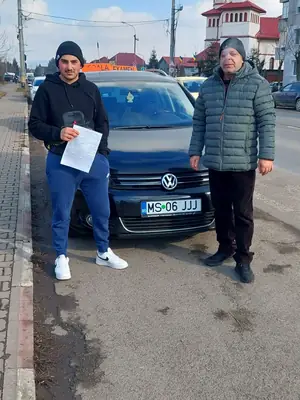 Cursant admis la examenul auto, cu foaia în mână, lângă mașina școlii
