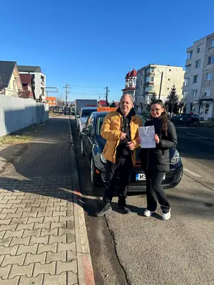 Cursant admis la examenul auto, cu foaia în mână, lângă mașina școlii