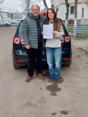 Cursant admis la examenul auto, cu foaia în mână, lângă mașina școlii