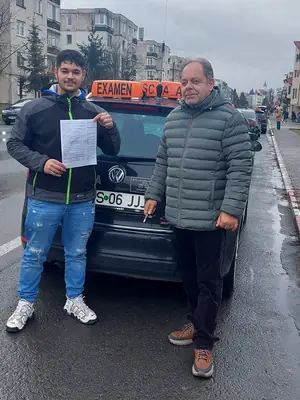 Cursant admis la examenul auto, cu foaia în mână, lângă mașina școlii