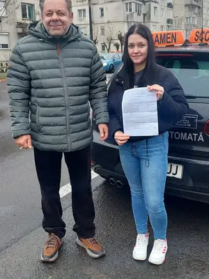 Cursant admis la examenul auto, cu foaia în mână, lângă mașina școlii