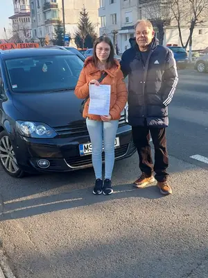 Cursant admis la examenul auto, cu foaia în mână, lângă mașina școlii