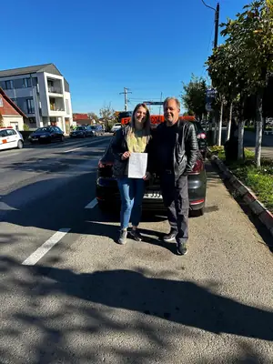 Cursant admis la examenul auto, cu foaia în mână, lângă mașina școlii