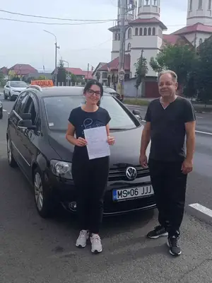 Cursant admis la examenul auto, cu foaia în mână, lângă mașina școlii