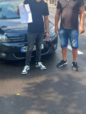 Cursant admis la examenul auto, cu foaia în mână, lângă mașina școlii